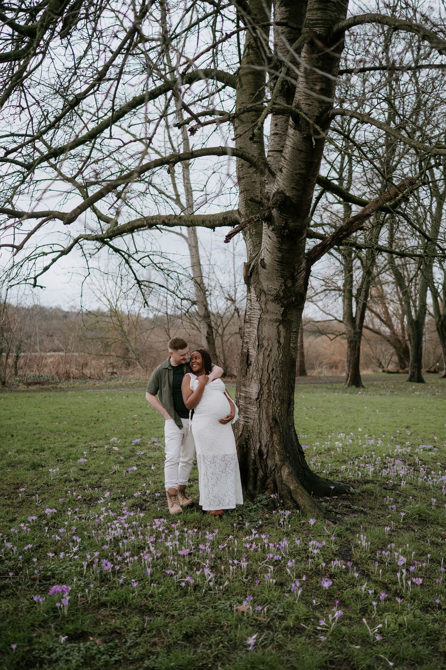 A couple shares tender moments among blooming purple crocuses in a wooded spring meadow.