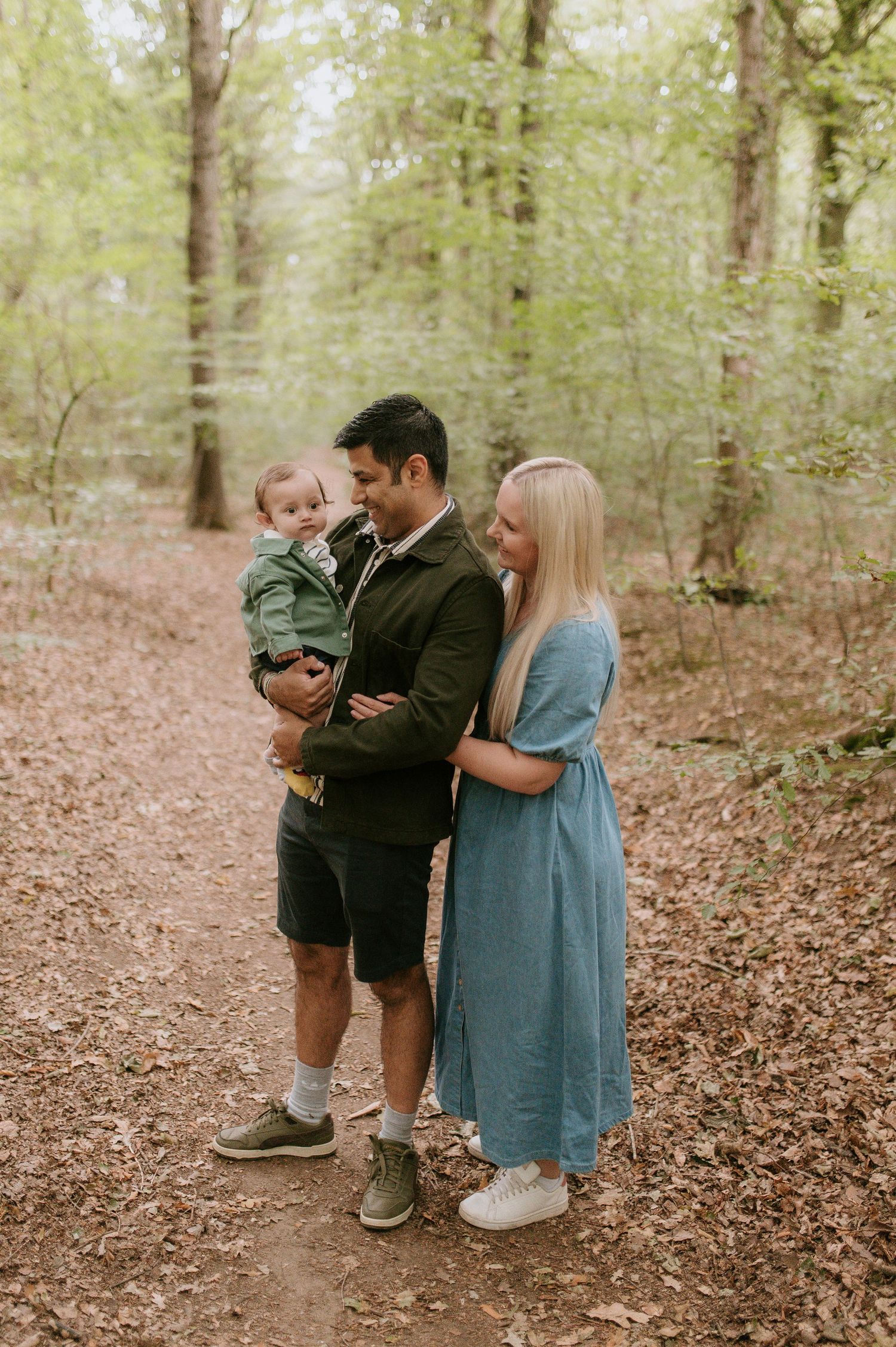 A family shares a tender moment together on a leaf-covered forest path during an autumn photo session.