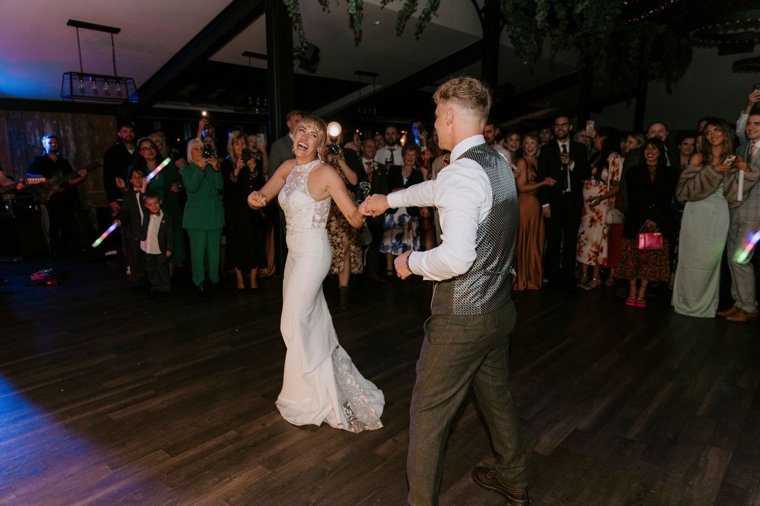 A couple shares a romantic dance on a dimly lit wooden dance floor at a wedding reception.