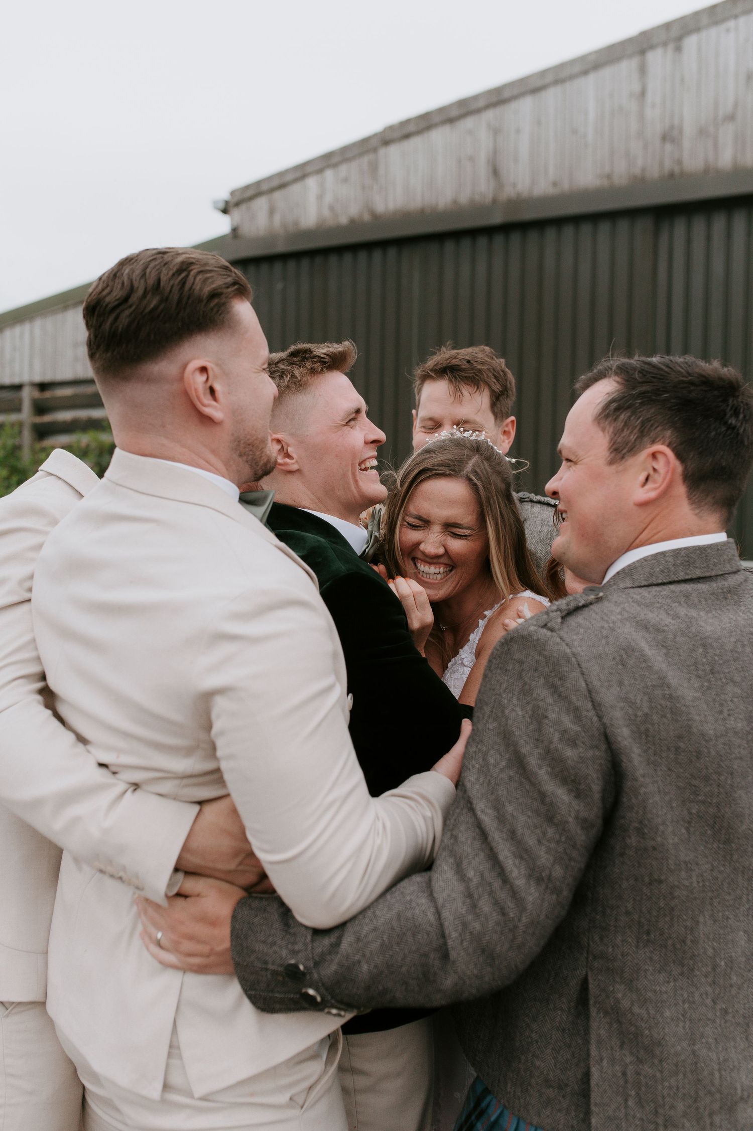 A candid group moment of wedding party members laughing together outside a building.