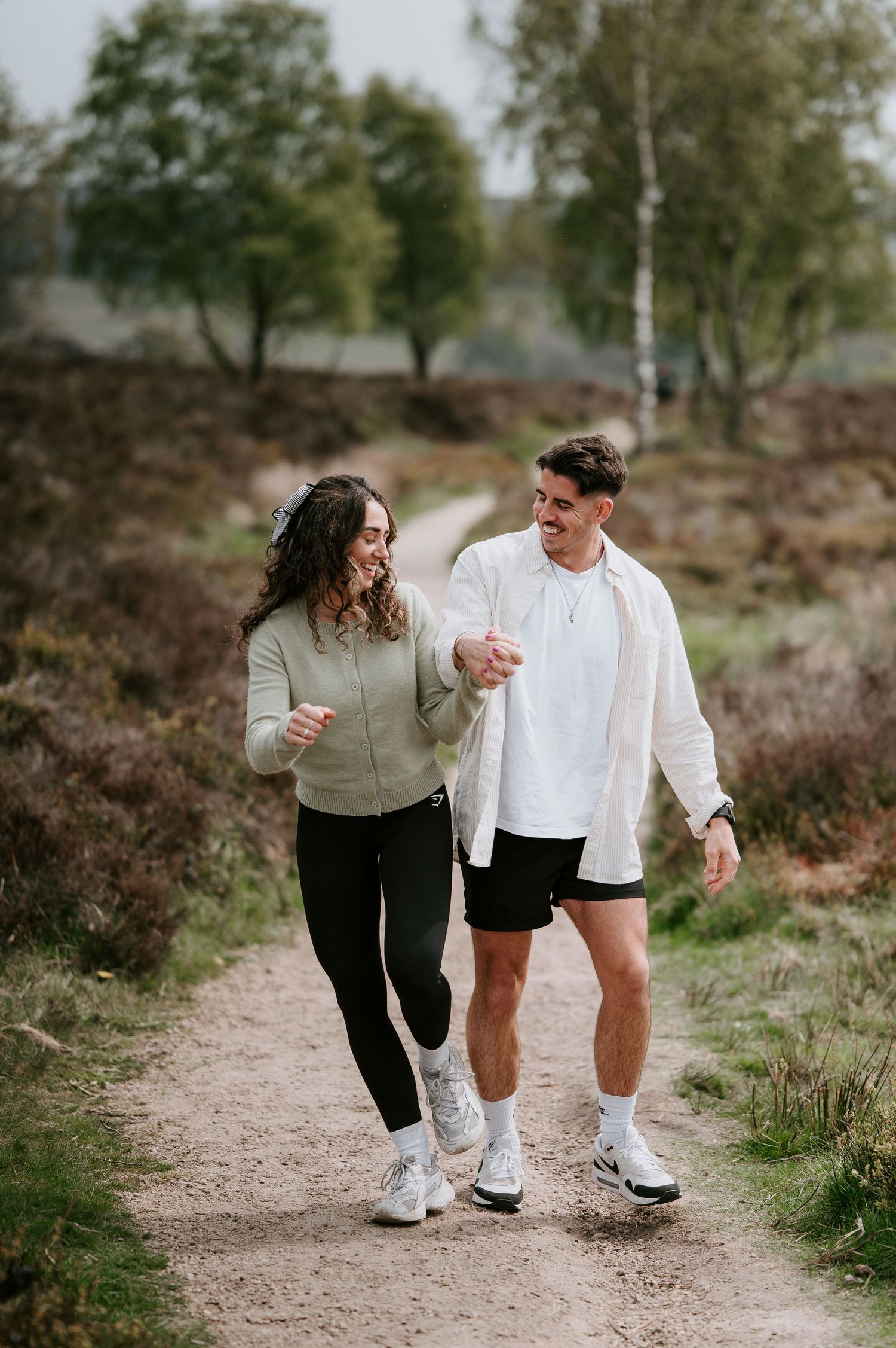 A couple walking and laughing together on a nature trail wearing casual white and black outfits.