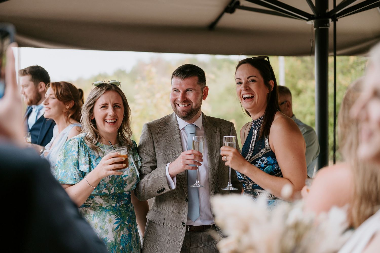 Wedding guests raise glasses in a toast during an outdoor celebration at a rustic venue.