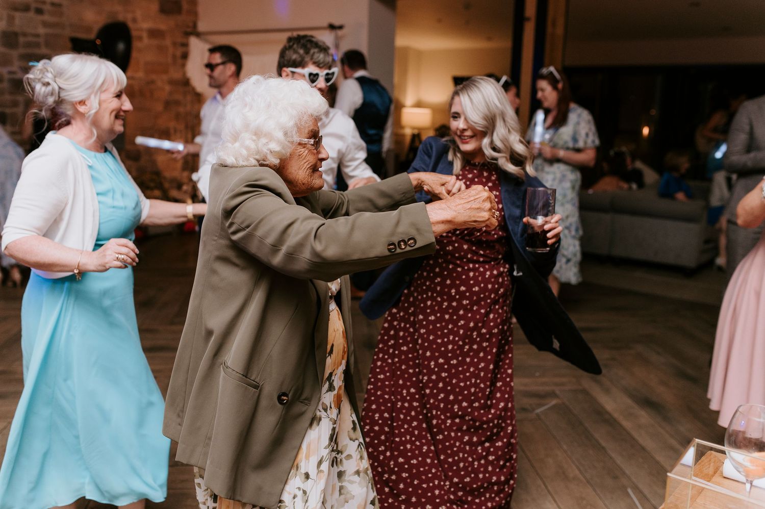 Couples dance together at a wedding reception in a rustic indoor venue with warm lighting.