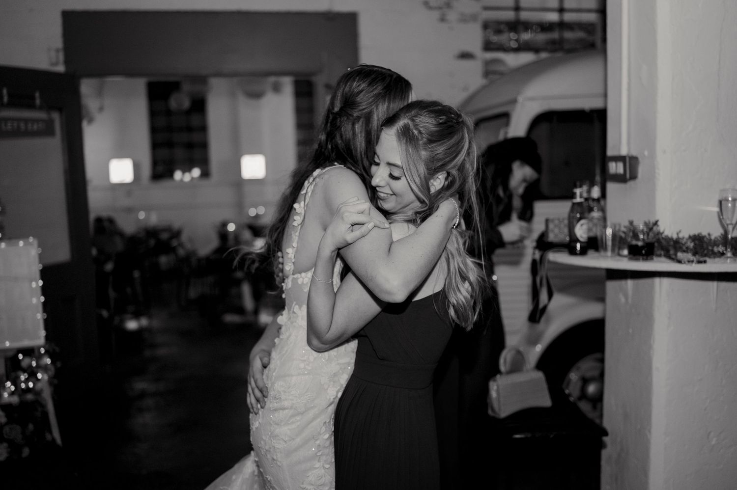 Bride shares emotional hug with guest in black and white wedding reception photo.