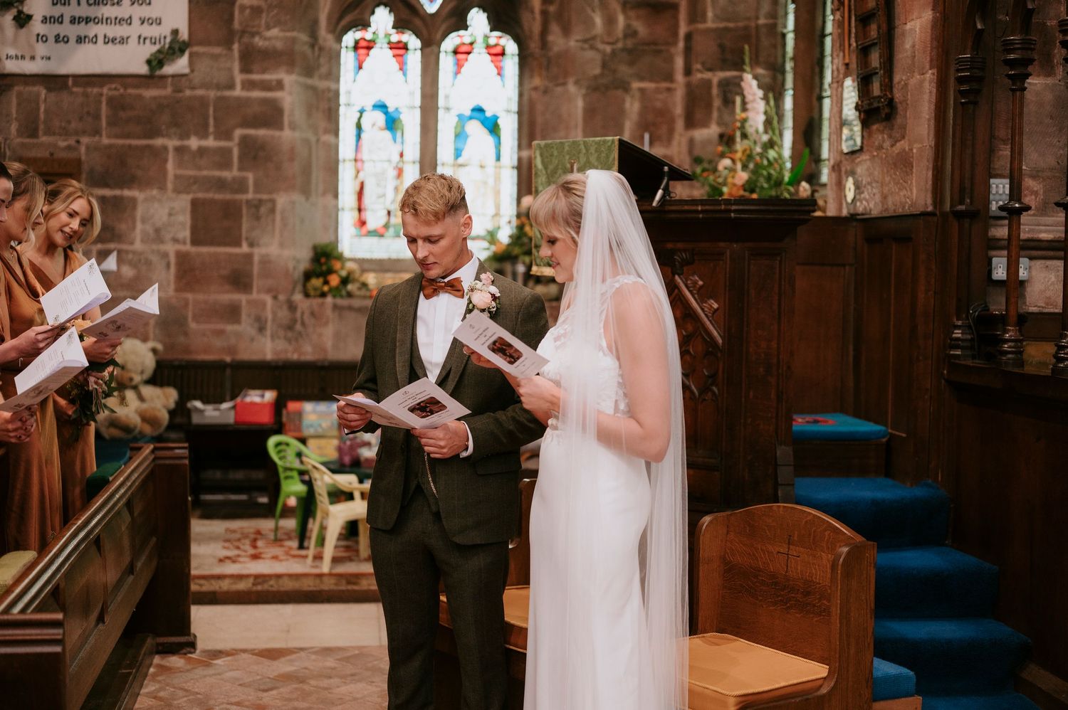 A couple exchanges vows during their wedding ceremony inside a traditional stone church with stained glass windows.