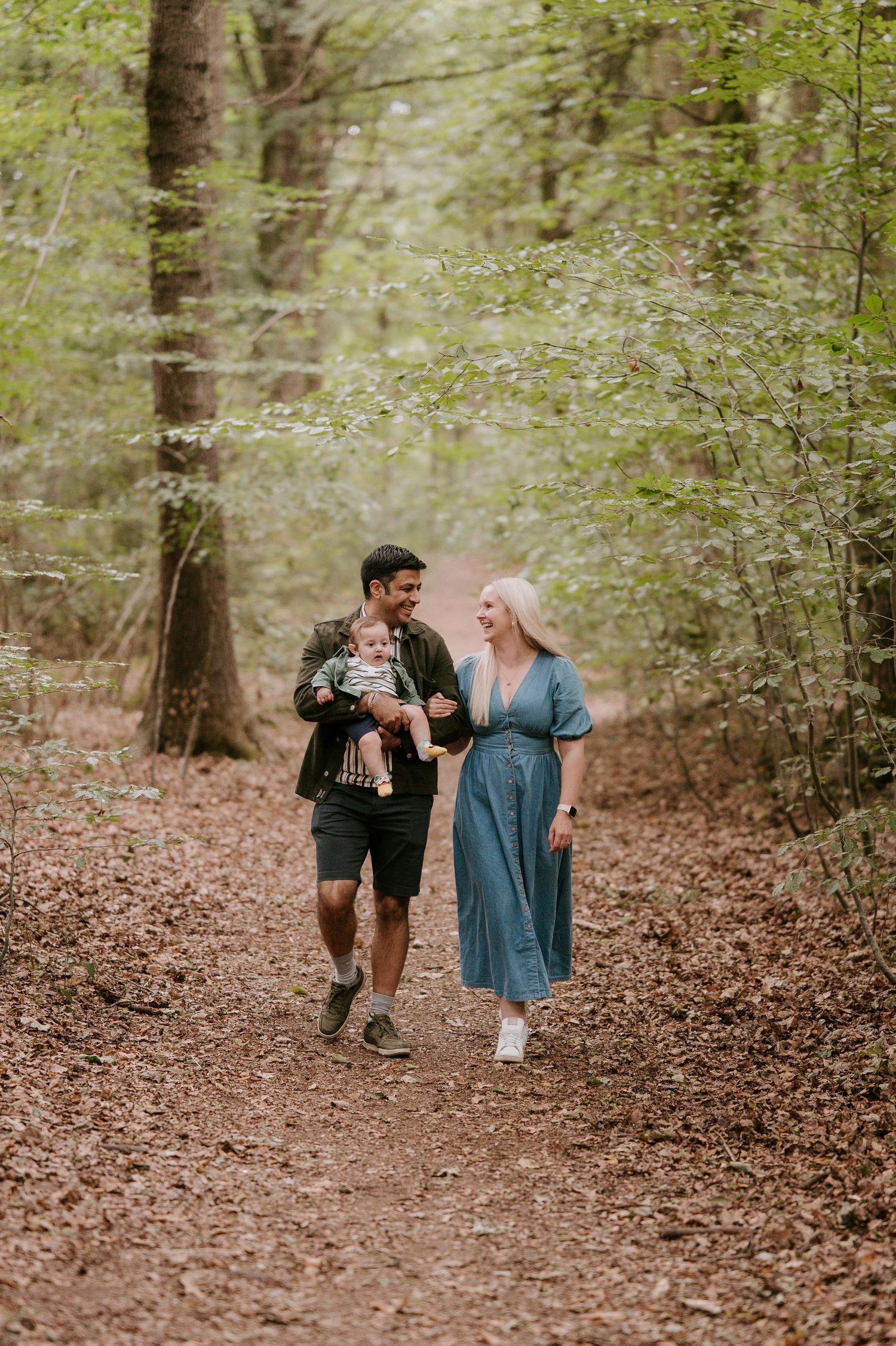 Three people walk together along a wooded trail covered in fallen leaves during an outdoor photo session.