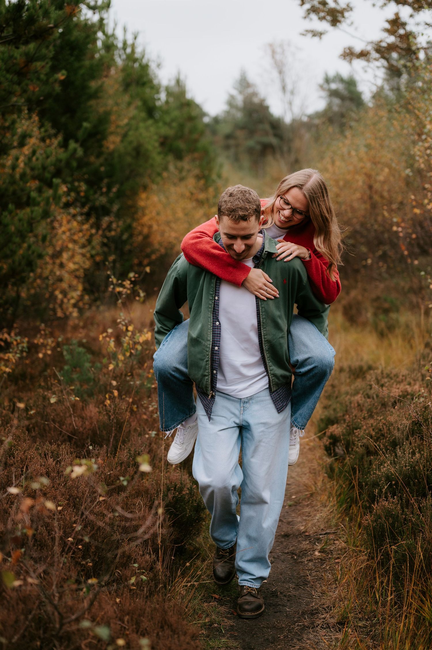 Two people share a playful moment together while walking along an autumn trail surrounded by fall foliage.