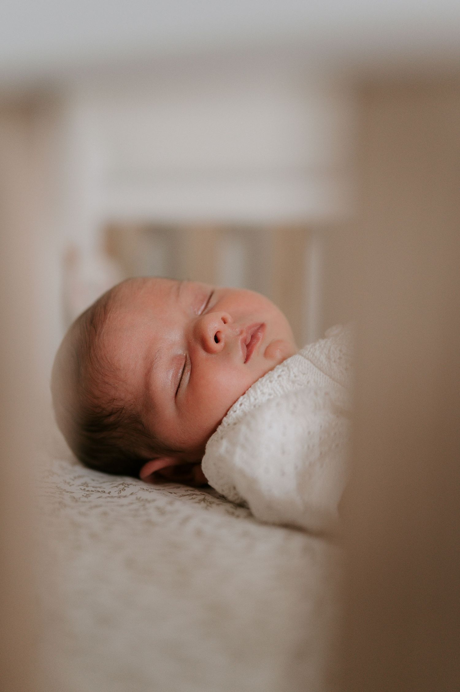 A sleeping newborn baby rests peacefully on soft white bedding in a serene portrait series.