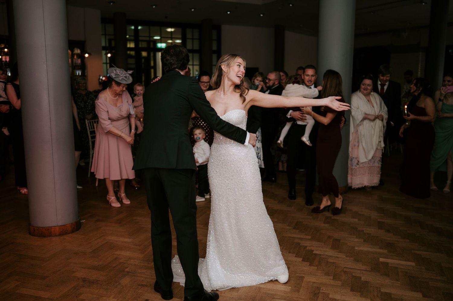 Wedding guests dance on a wooden floor during evening reception celebrations.