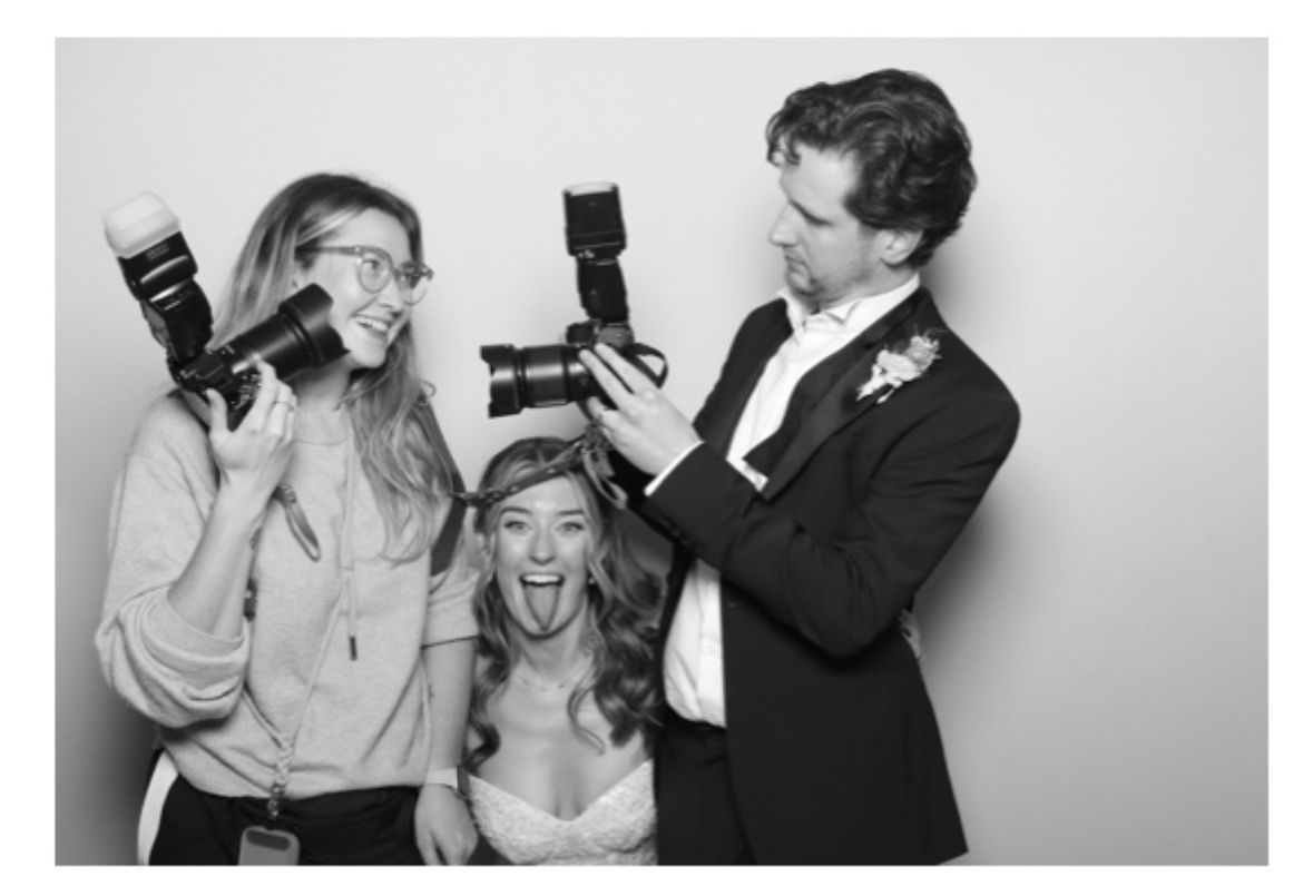 Three photographers pose playfully with their cameras in a black and white photo.