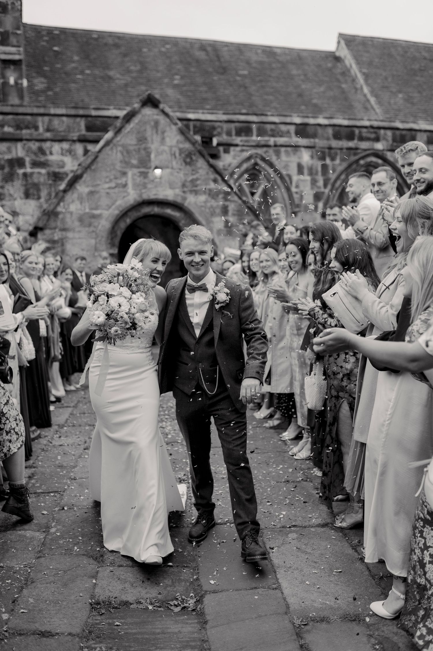 Wedding guests form a line to shower the happy couple with confetti in this black and white celebration sequence.