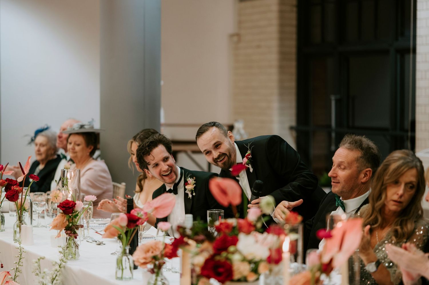 Wedding guests seated at long tables decorated with pink and white floral centerpieces.