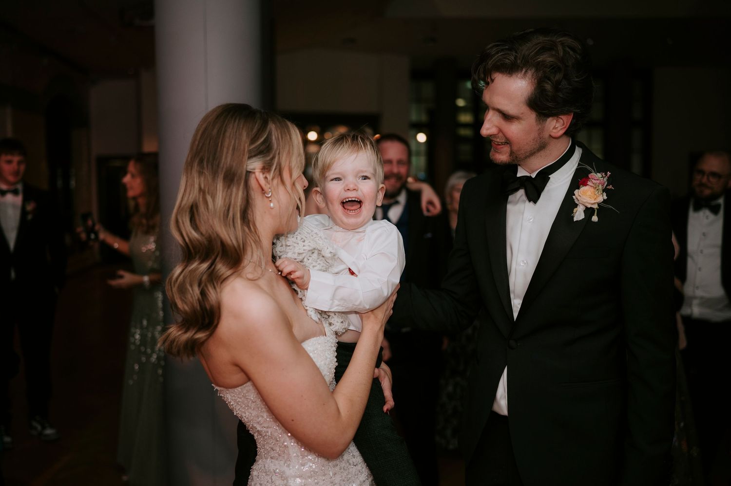 A tender family moment during a wedding reception with formal attire and dim lighting.