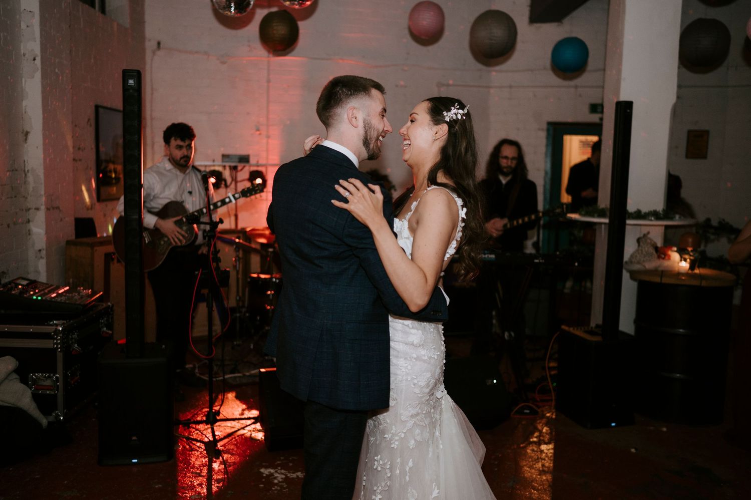 Bride and groom share first dance at wedding reception with live band performing in background.