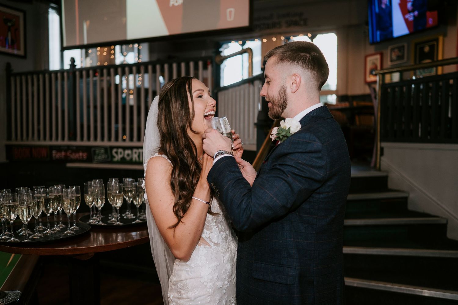 Bride and groom share a joyful moment with champagne glasses at their wedding reception in an elegant venue.