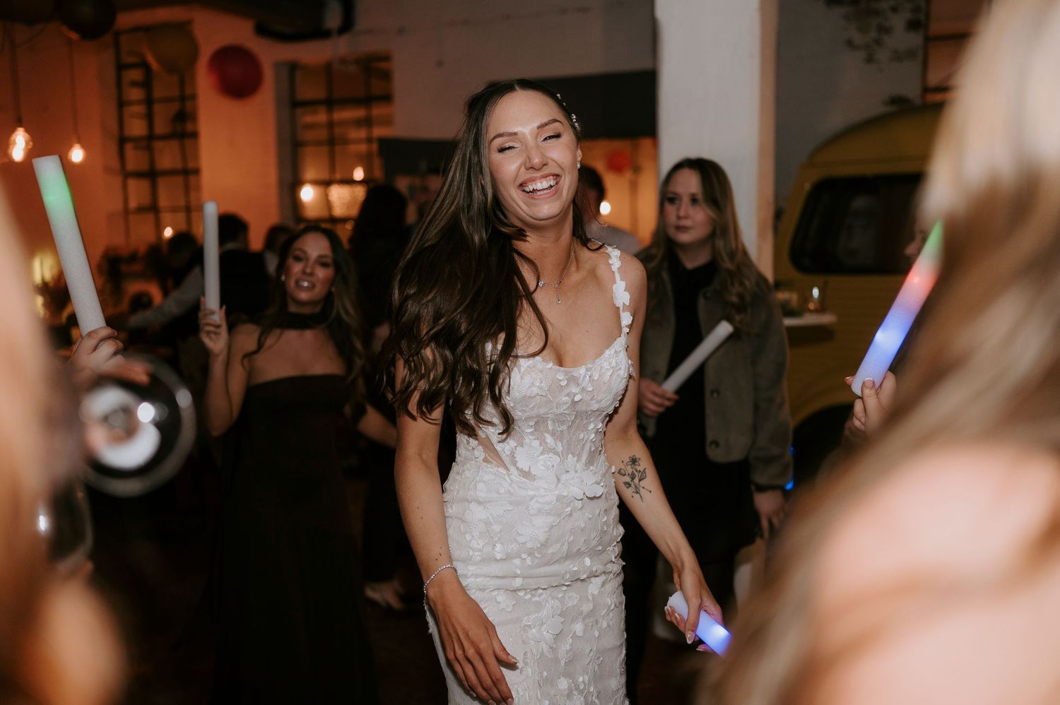 Beautiful bride in fitted lace gown smiling while dancing surrounded by guests with glow sticks.