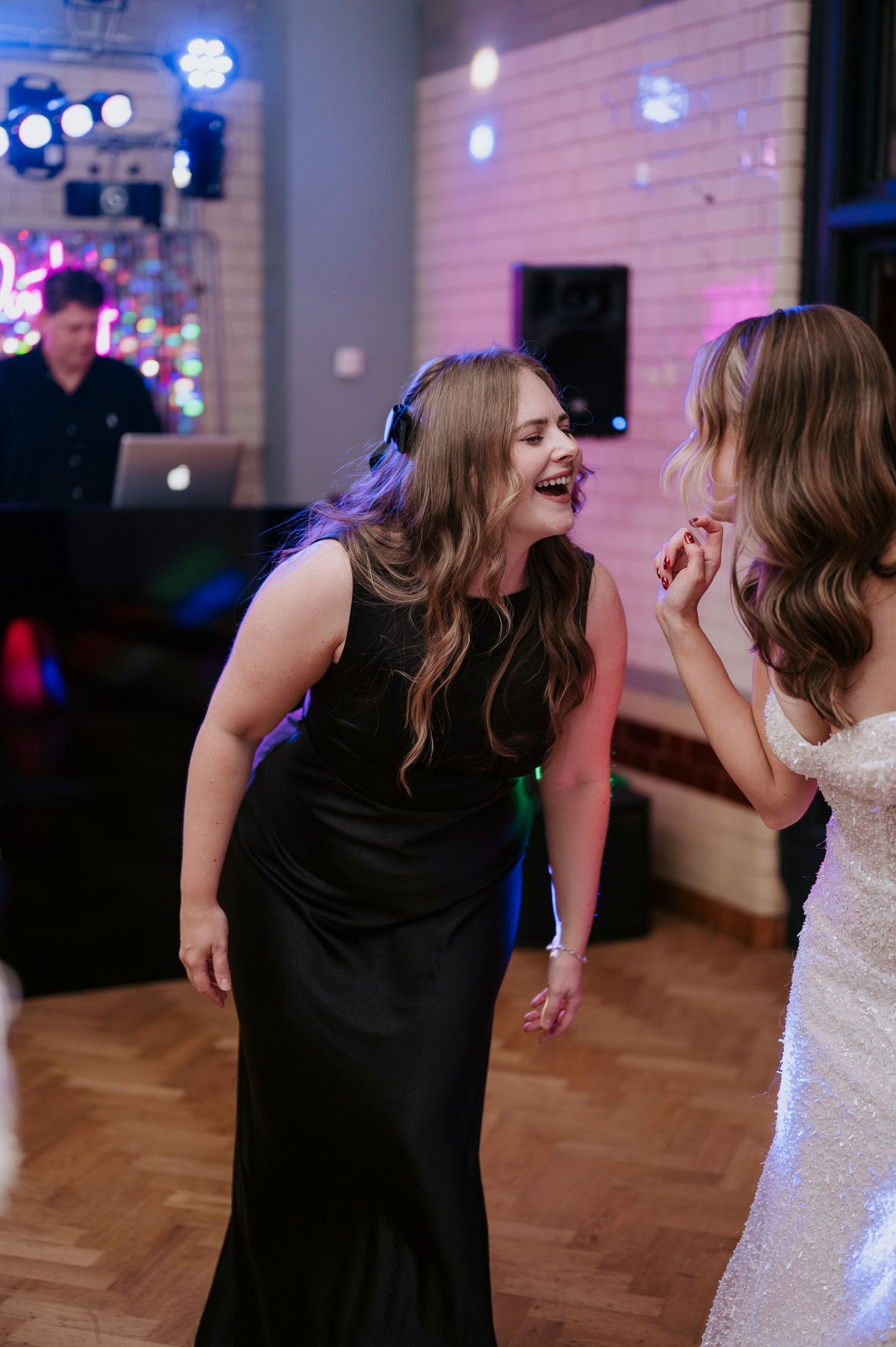 Two people in formal attire sharing laughter on a dance floor with colorful lighting.