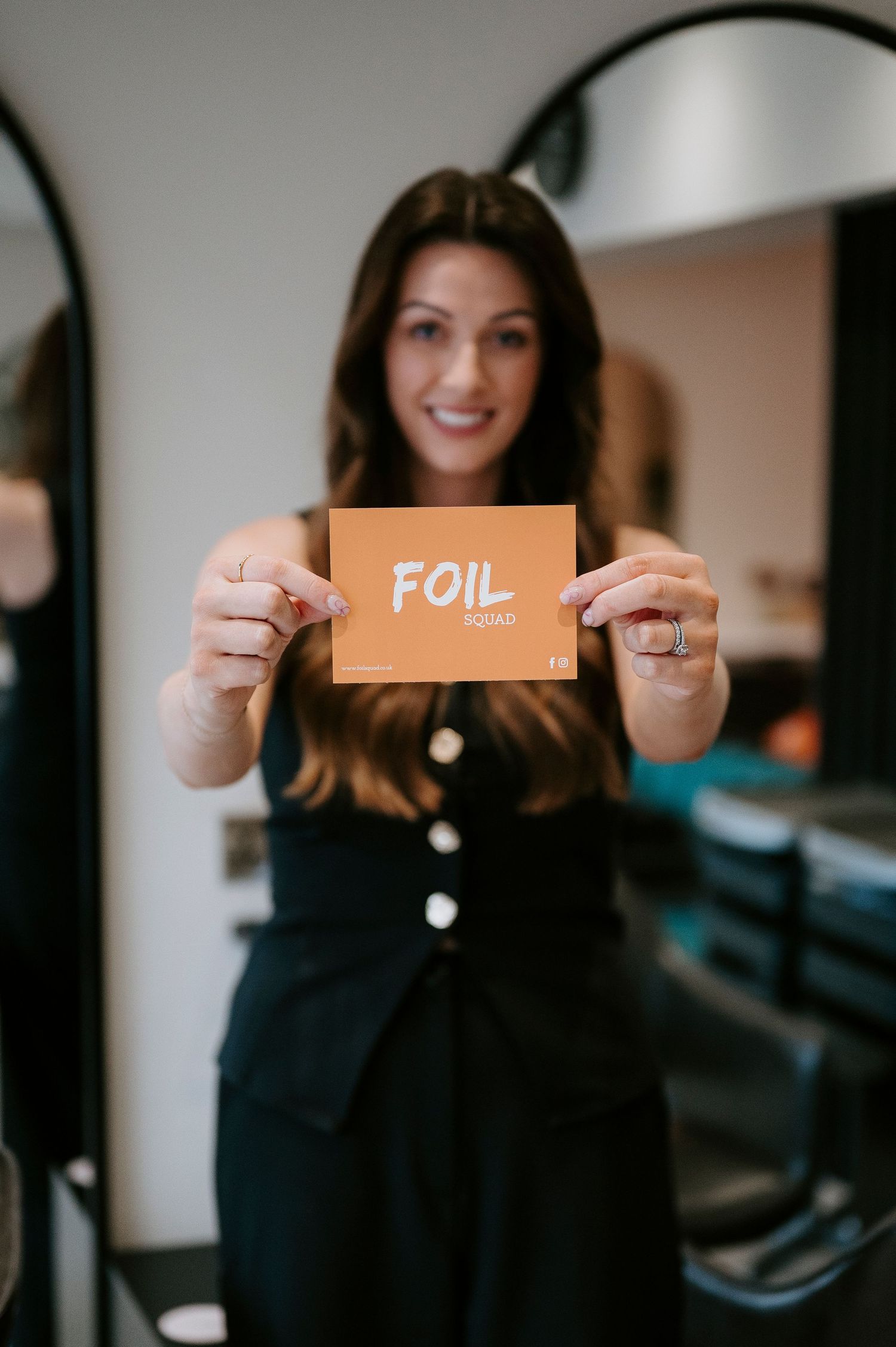 Person in dark clothing holds up orange paper signs while smiling in front of white wall.