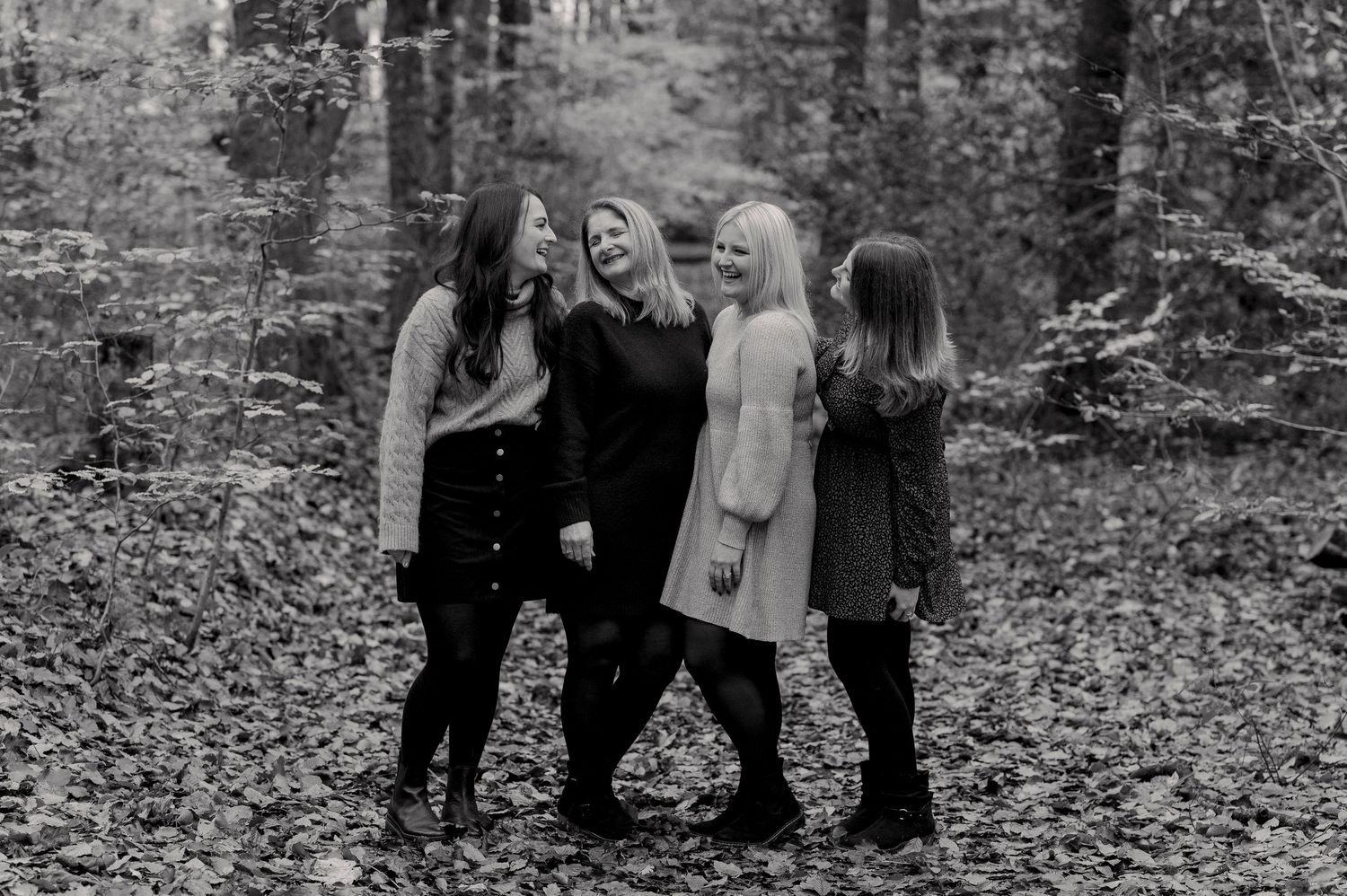 Four friends sharing laughter together in a black and white autumn forest scene.