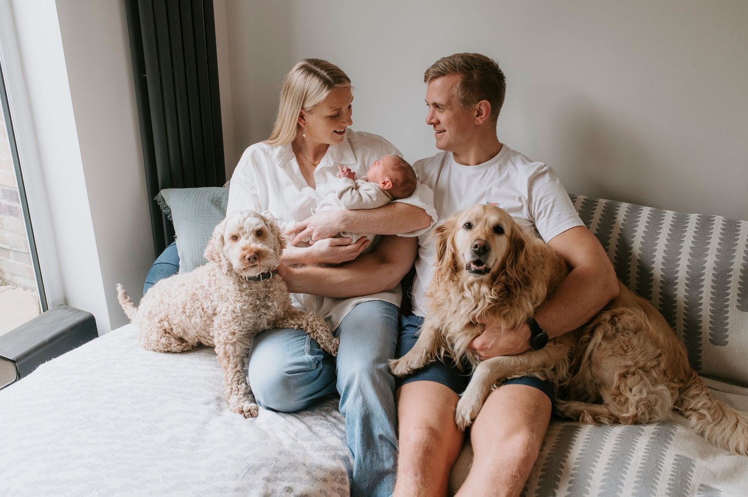 Family relaxing on couch at home with their newborn baby and two friendly dogs.