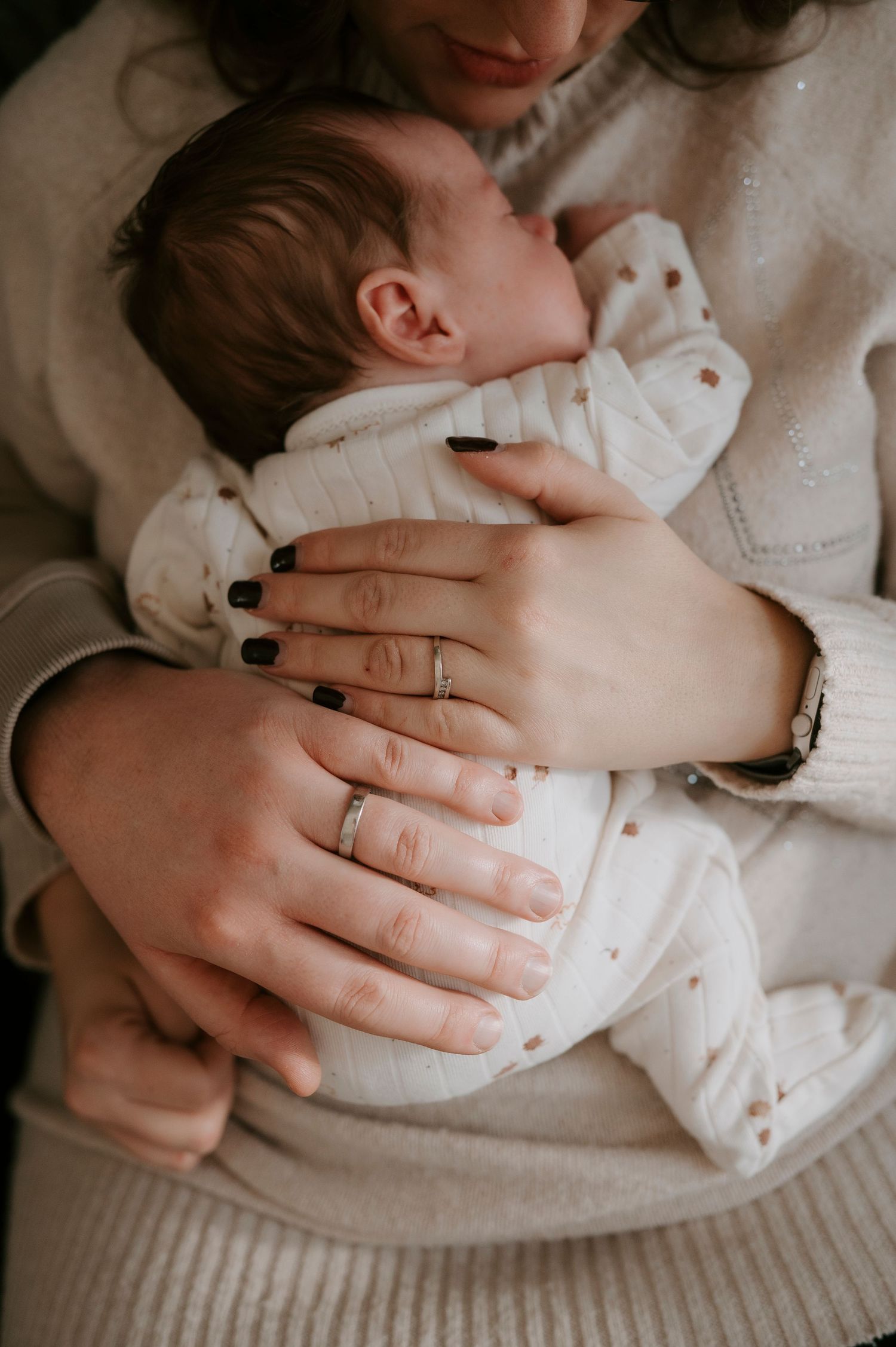 A series of intimate black and white photos showing hands gently cradling a newborn baby in soft white fabric.