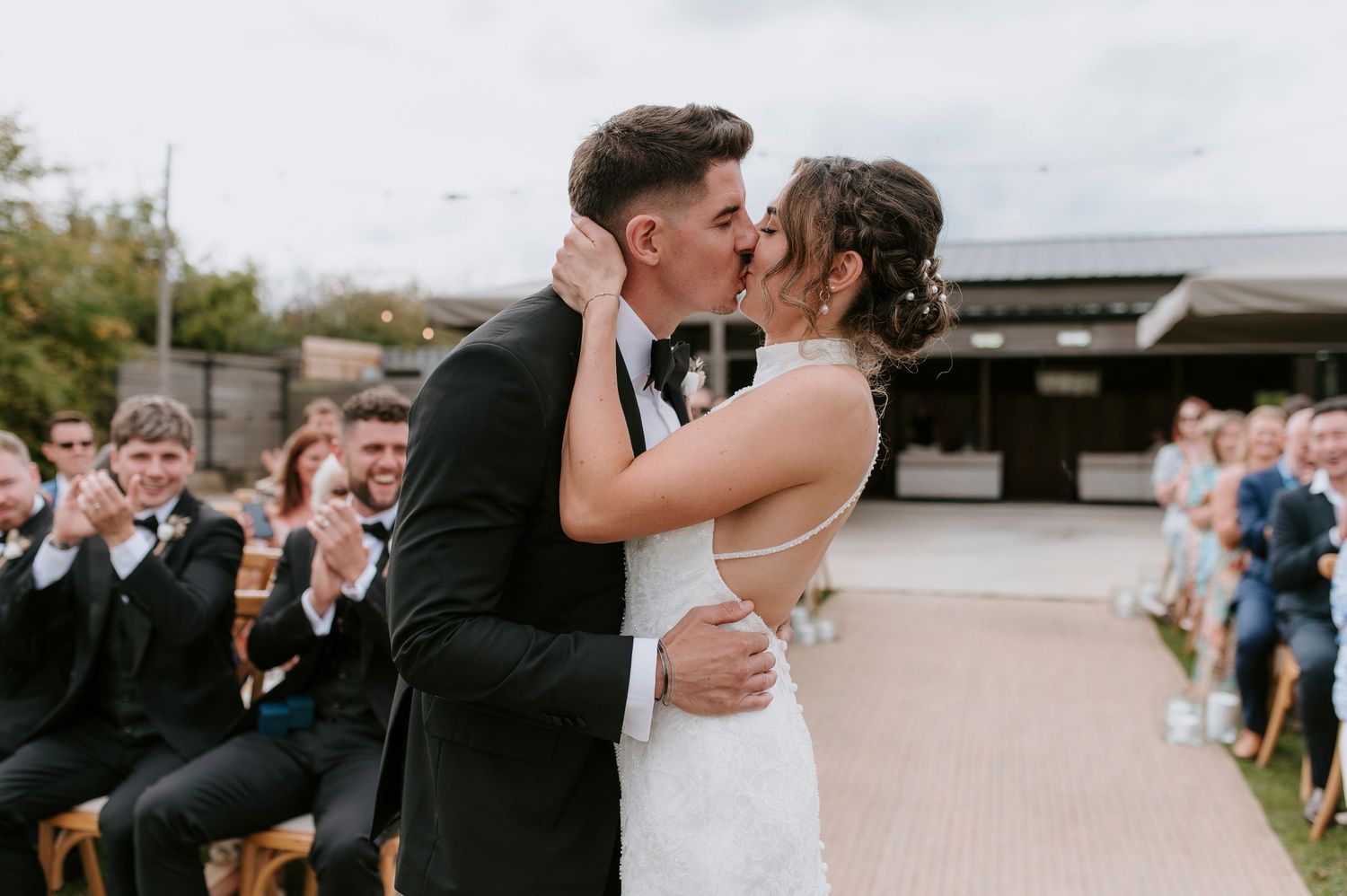 A couple shares romantic kisses during their wedding celebration in multiple candid moments outdoors.