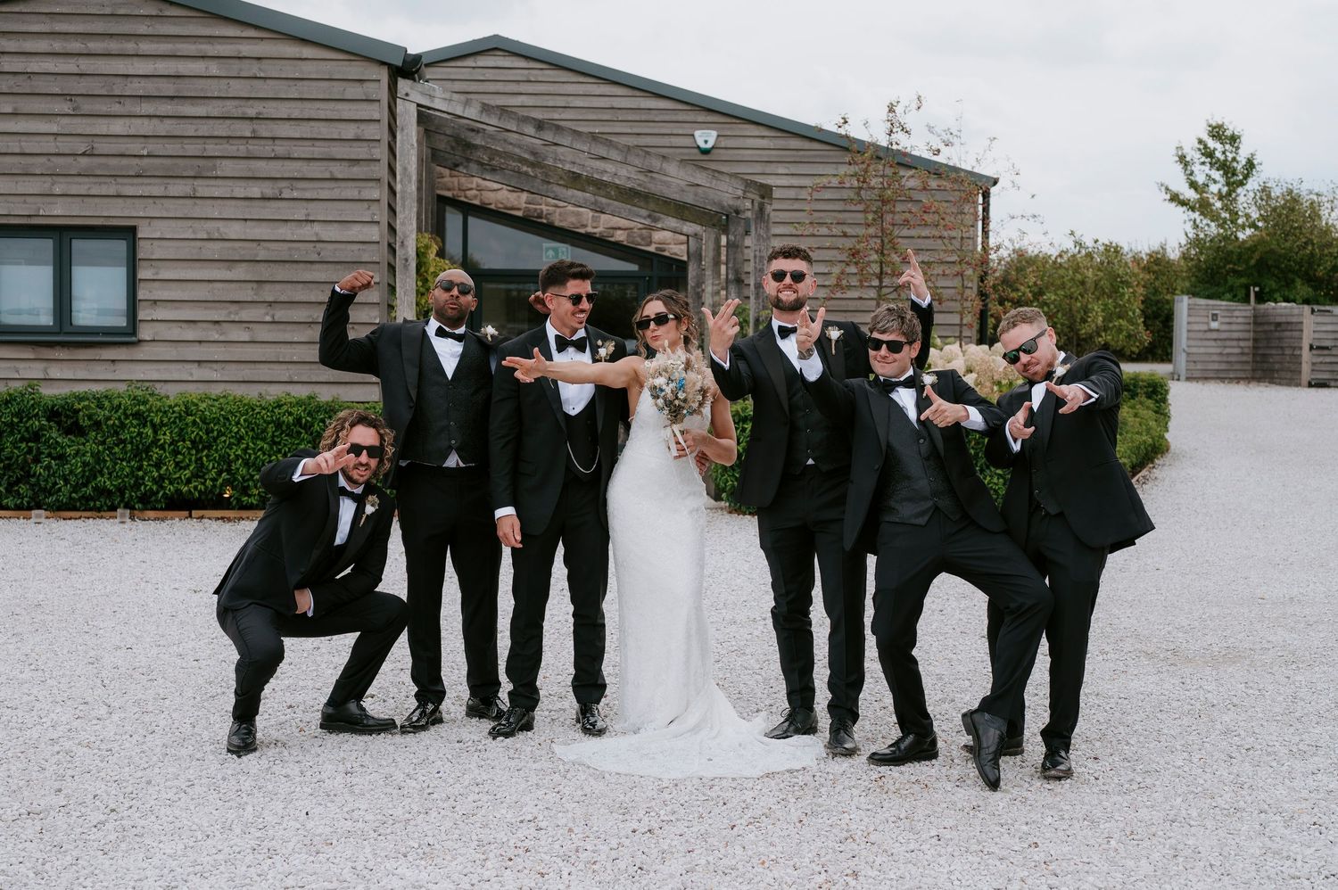 Wedding party in formal attire poses laying on white ground in creative formation outside venue.