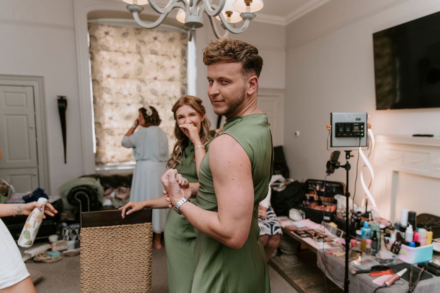 People getting ready in a casual living room setting with makeup and styling tools scattered around.