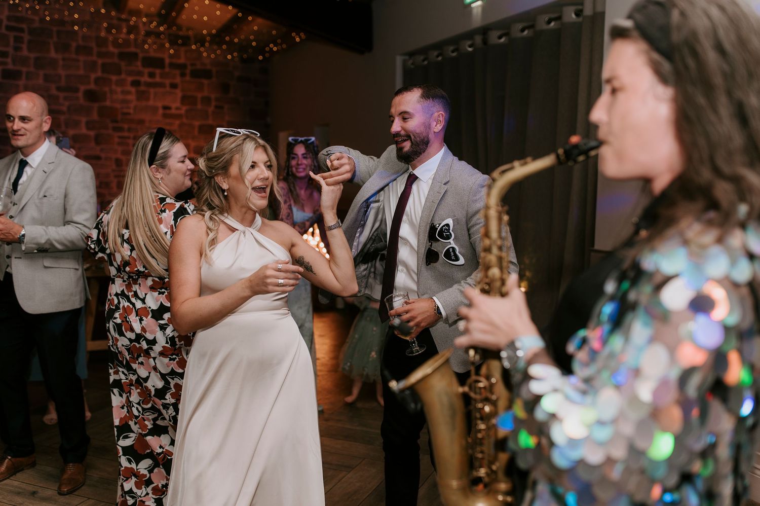 Wedding guests dancing and celebrating together on a dark dance floor with brick walls in the background.
