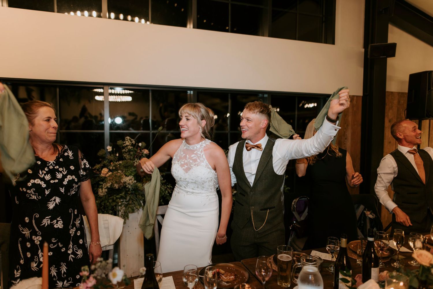 Wedding guests celebrate and dance together during a reception dinner at an indoor venue.