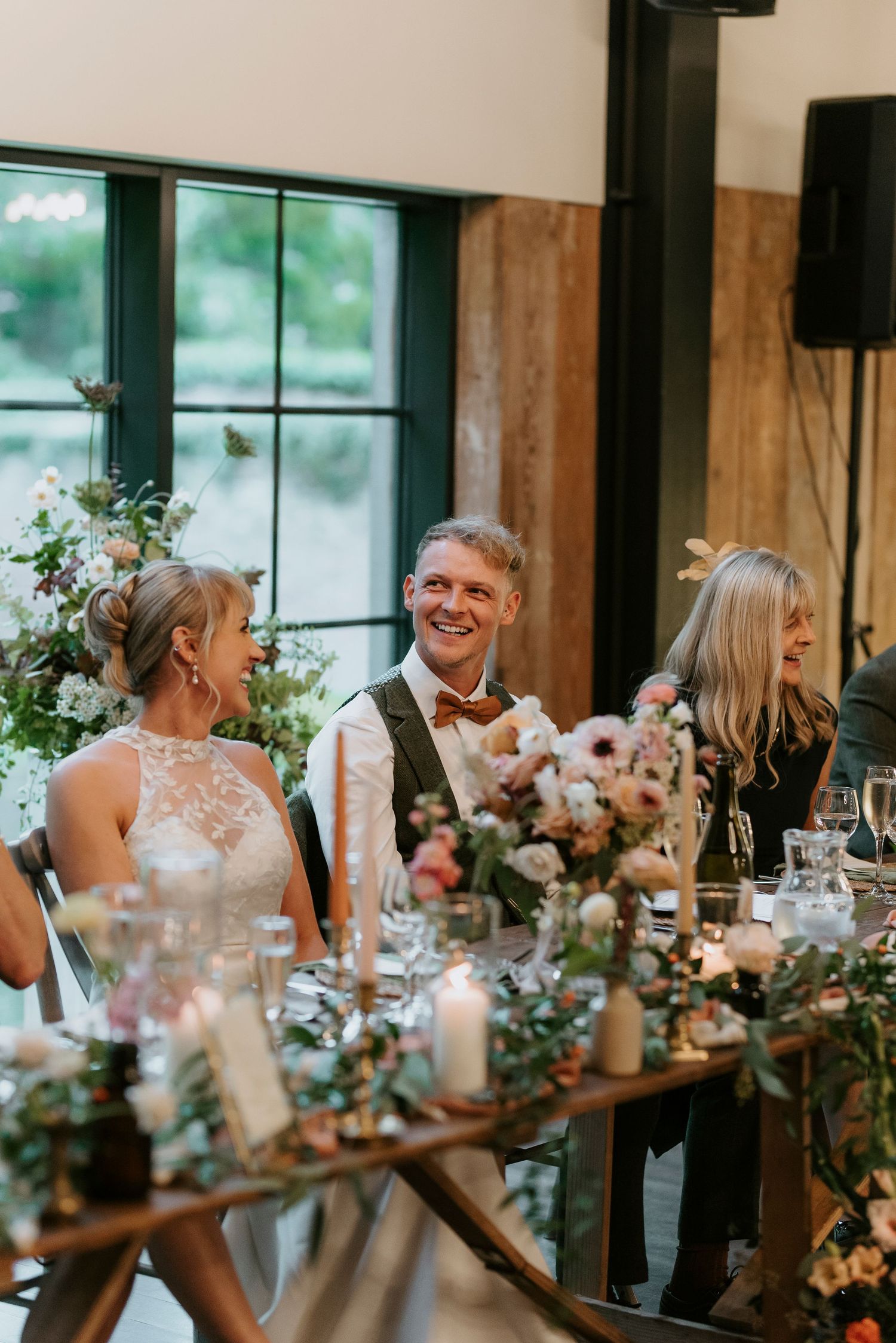 Wedding reception dinner table decorated with elegant floral centerpieces and candlelight in a rustic venue.