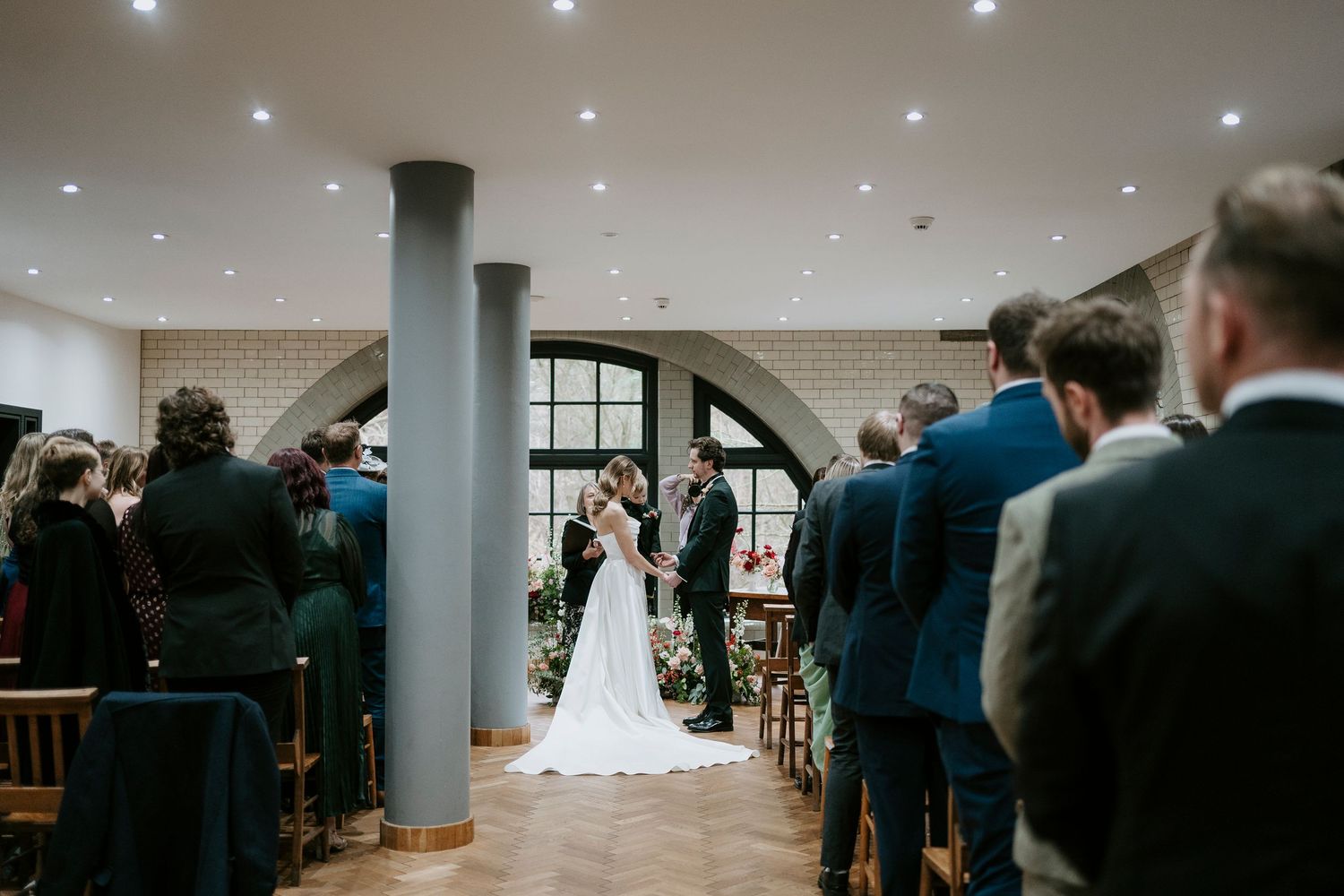 Wide view of a wedding ceremony in a contemporary space with white columns and recessed lighting.
