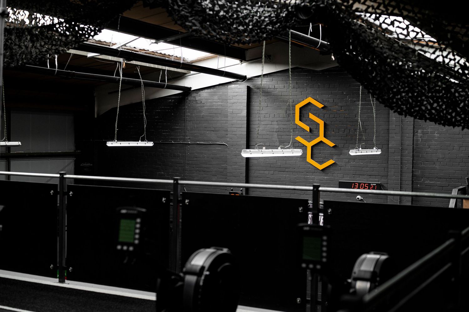 Dark gym interior with suspended lighting and yellow signage visible on the walls.