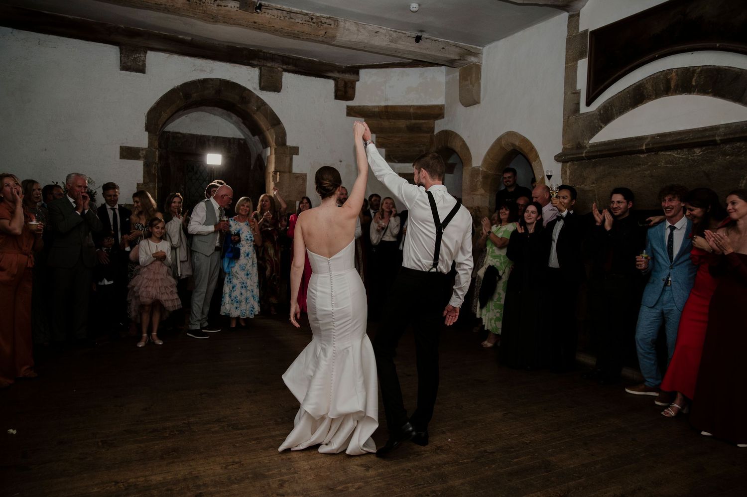 Wedding reception dance floor scene with guests celebrating in a dimly lit venue.