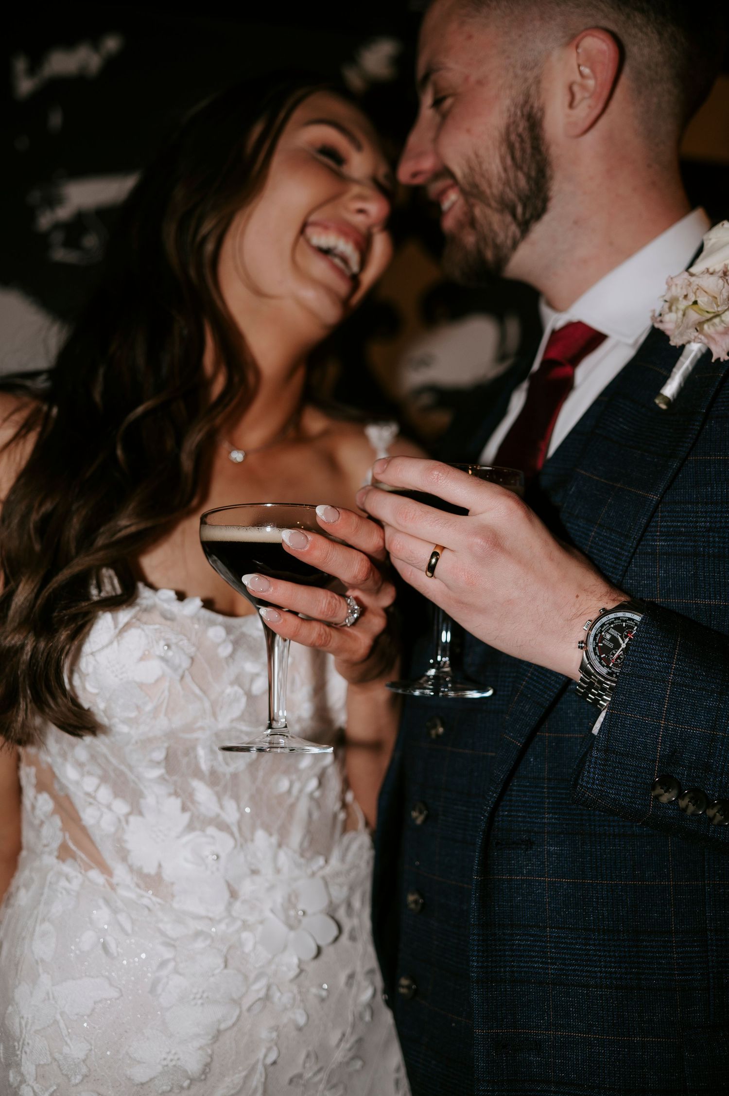 Laughing bride and groom toast with wine glasses at their wedding reception.