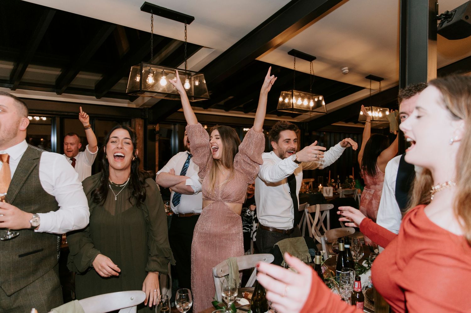 A group of wedding guests dancing and celebrating on a dimly lit dance floor at a reception party.