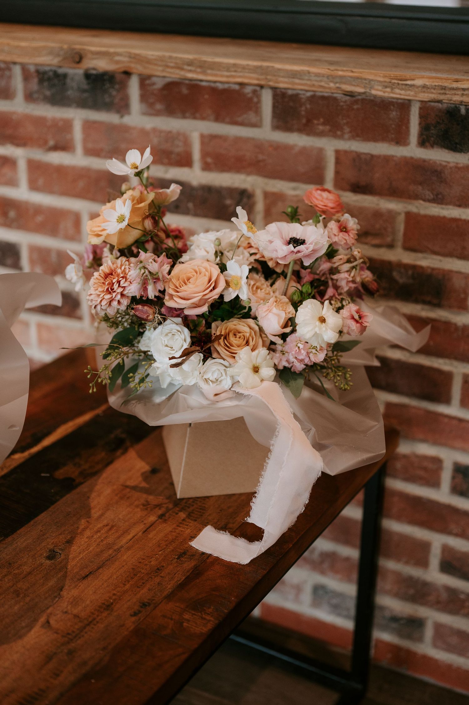 A series of floral arrangements with peach and pink blooms displayed on a wooden bench against a brick wall.