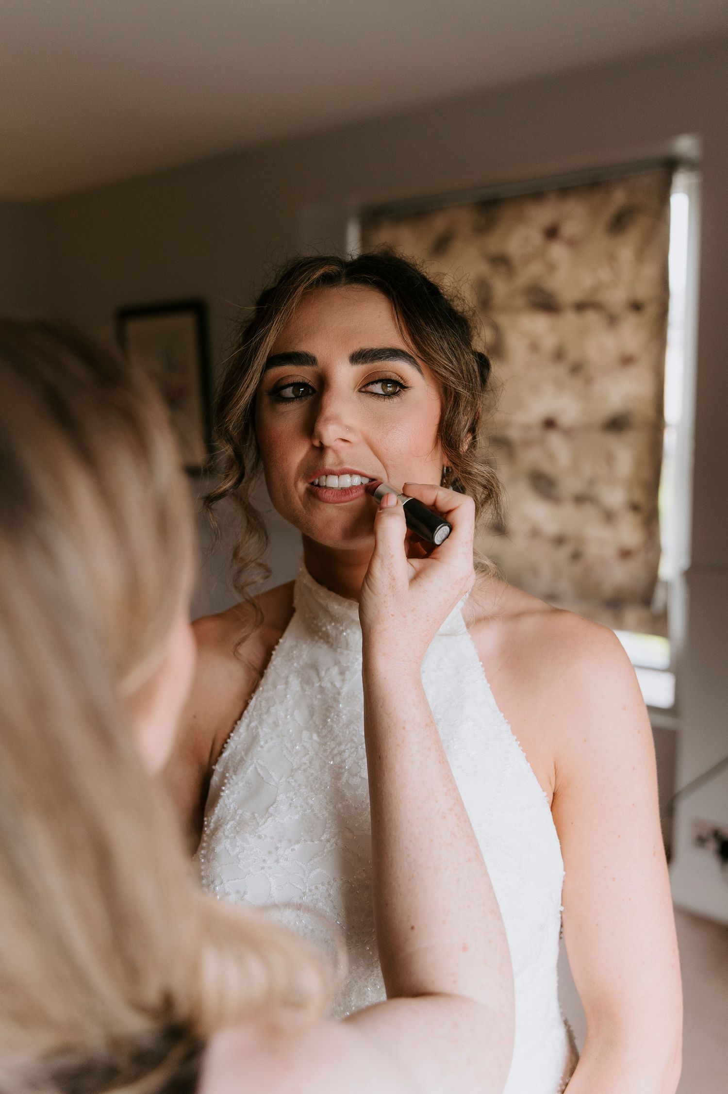A bride in a white lace wedding dress laughs joyfully while getting ready for her special day.