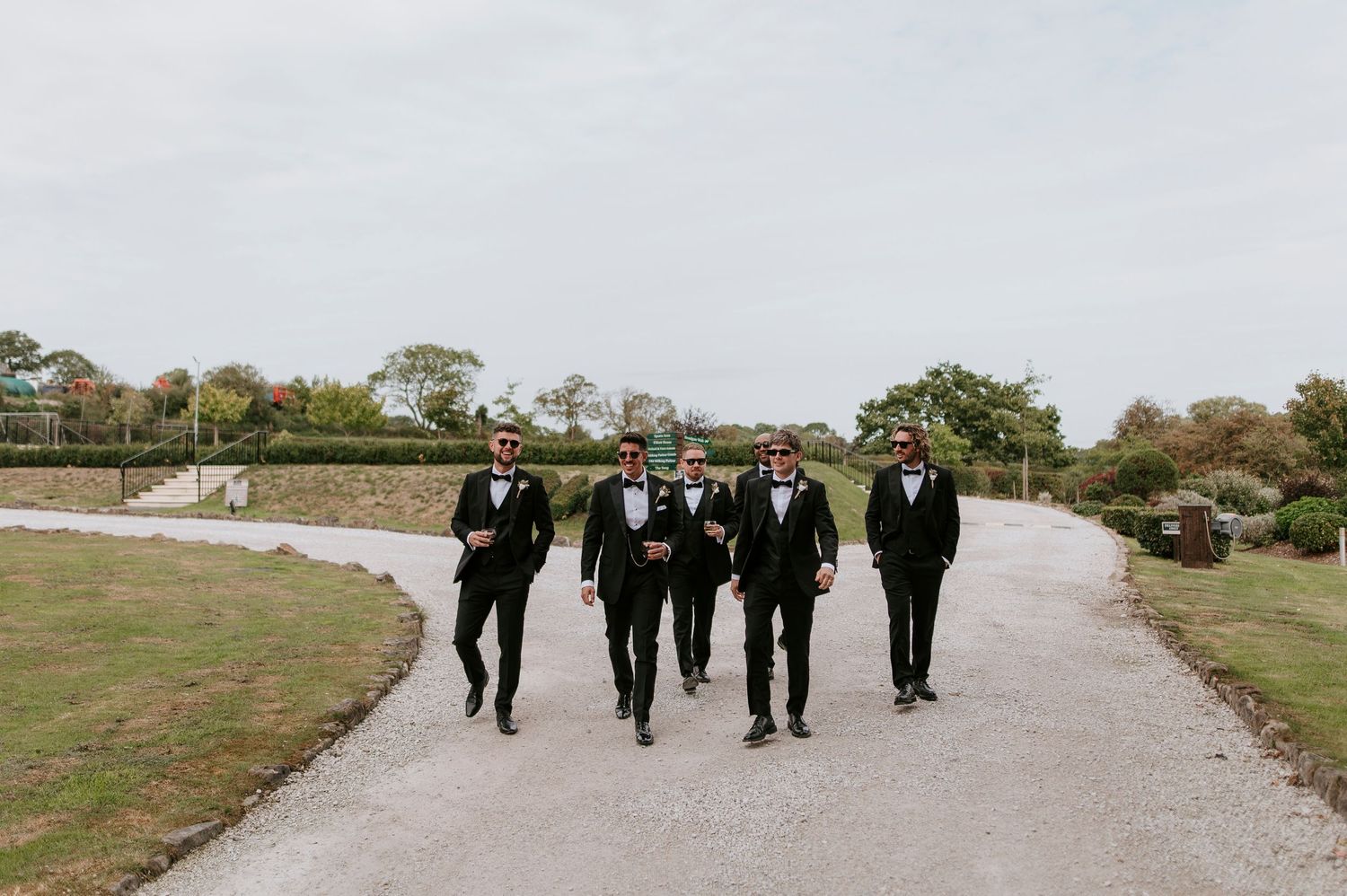 Wedding party walking along a stone path through a grassy landscape at sunset.