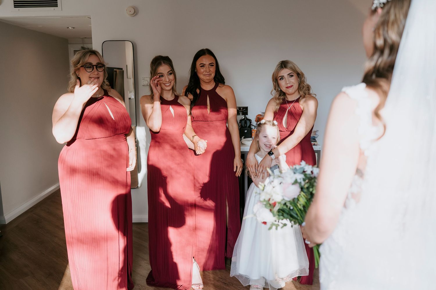 Emotional bridesmaids in coral dresses react with tears and joy as bride in white gown reveals her wedding look.