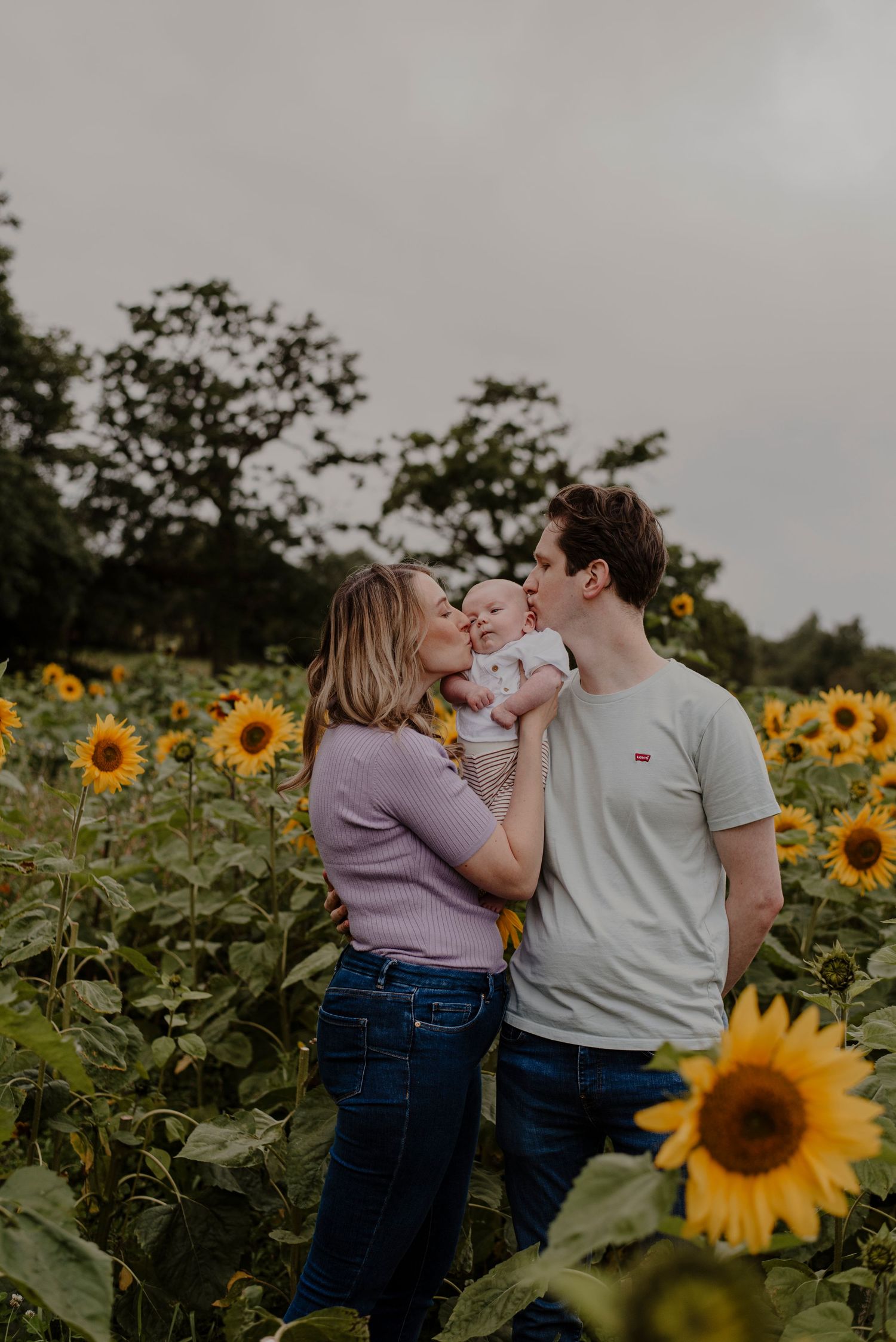 A couple shares a playful moment in a vibrant sunflower field at dusk.