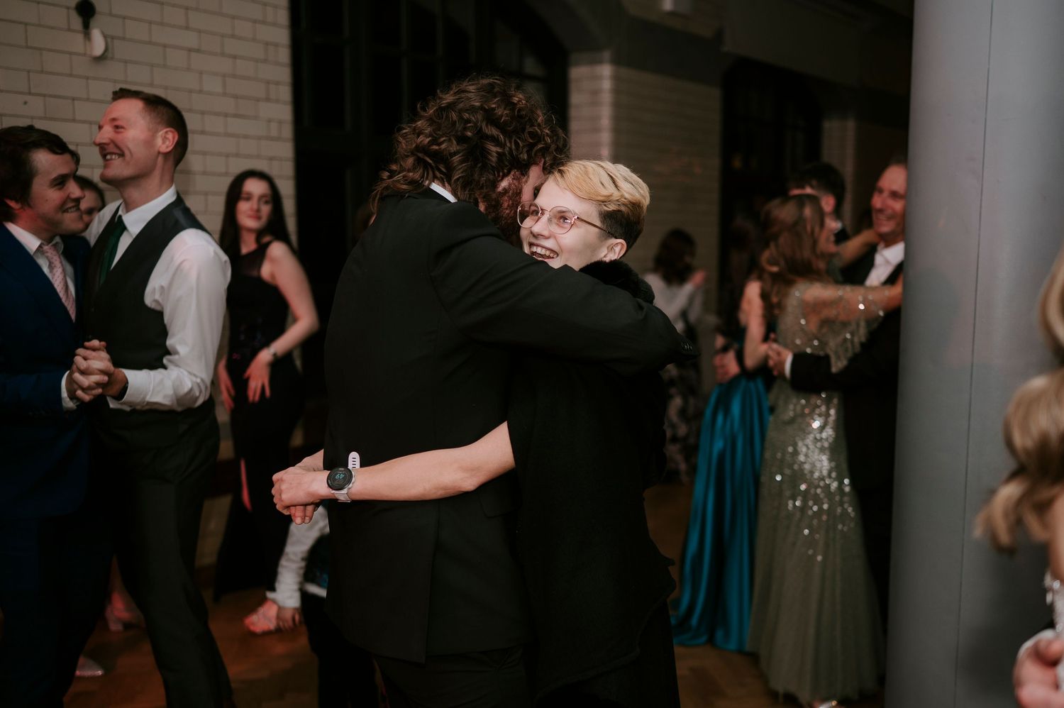 Wedding guests dancing and celebrating in a dimly lit reception venue with brick walls.