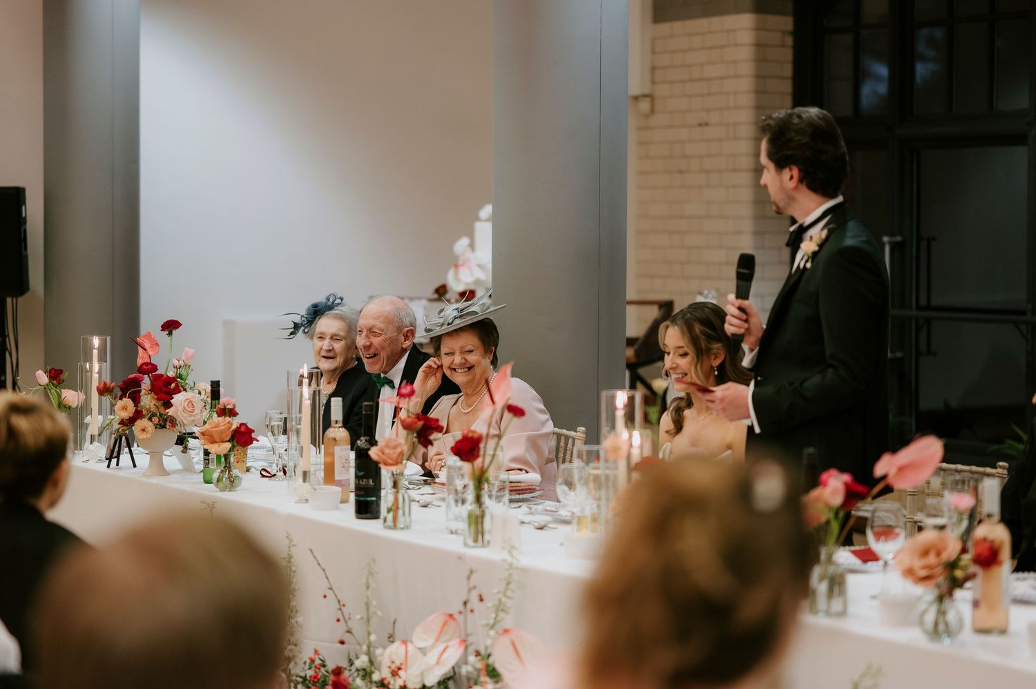 Long banquet tables set for a wedding reception with red floral centerpieces and white linens.