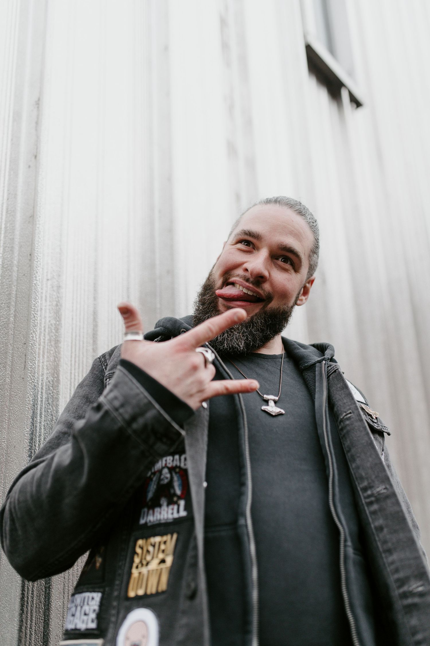 Smiling person in black jacket making hand gestures against white wall background.