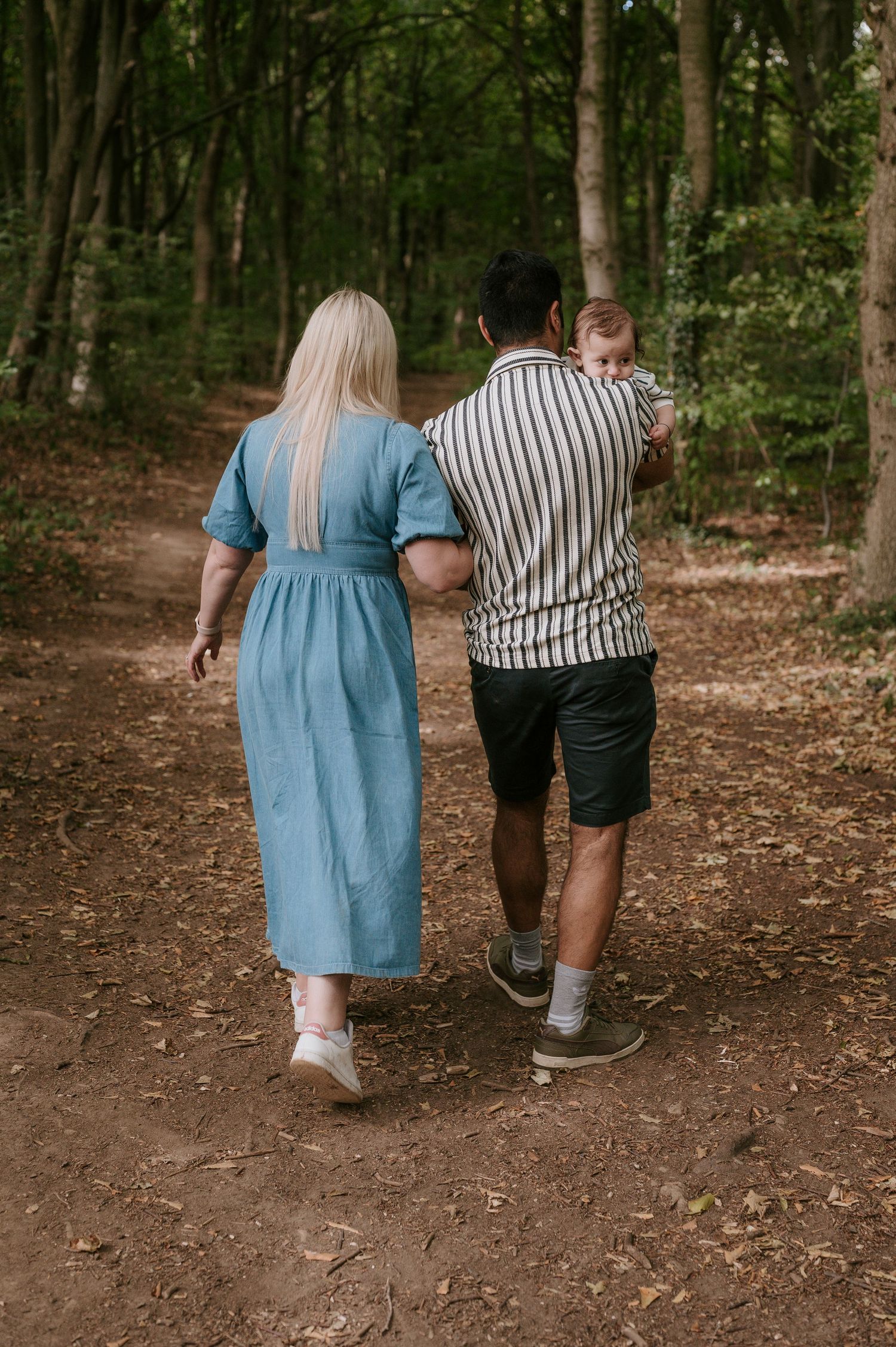 A couple walking together through a forest path holding hands during an outdoor photo session.