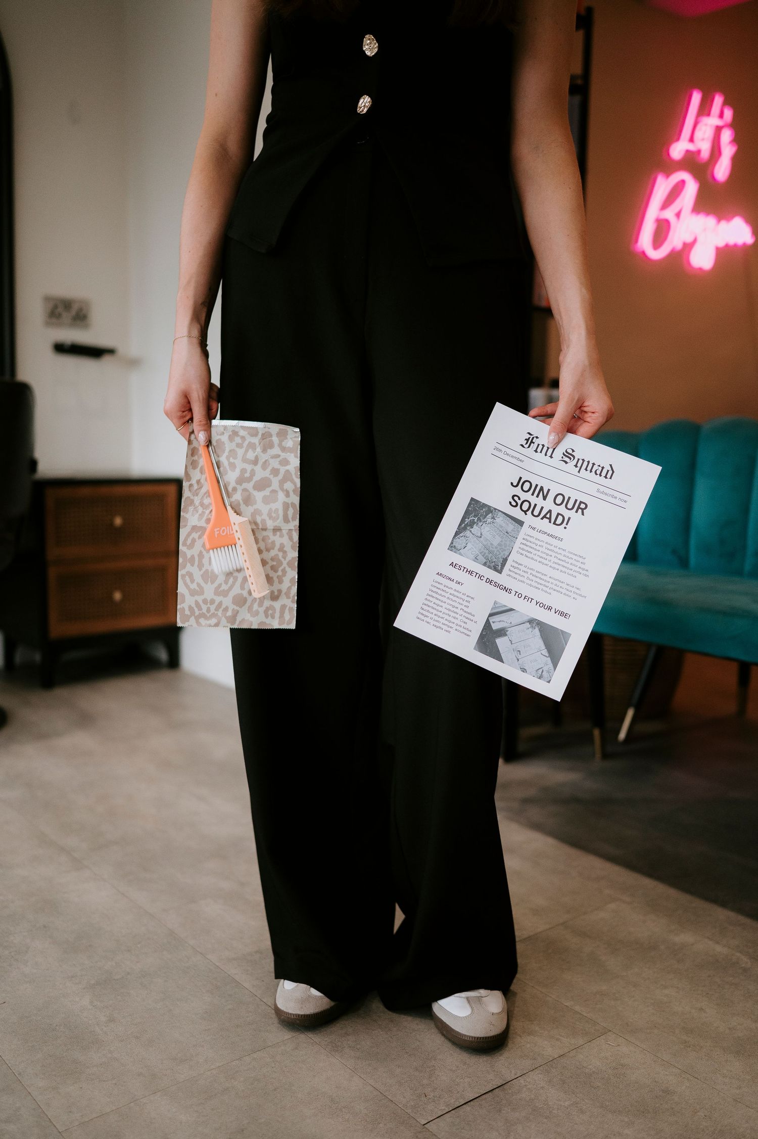 Person in black outfit holding a newspaper and small bag stands near pink neon signage in an interior space.