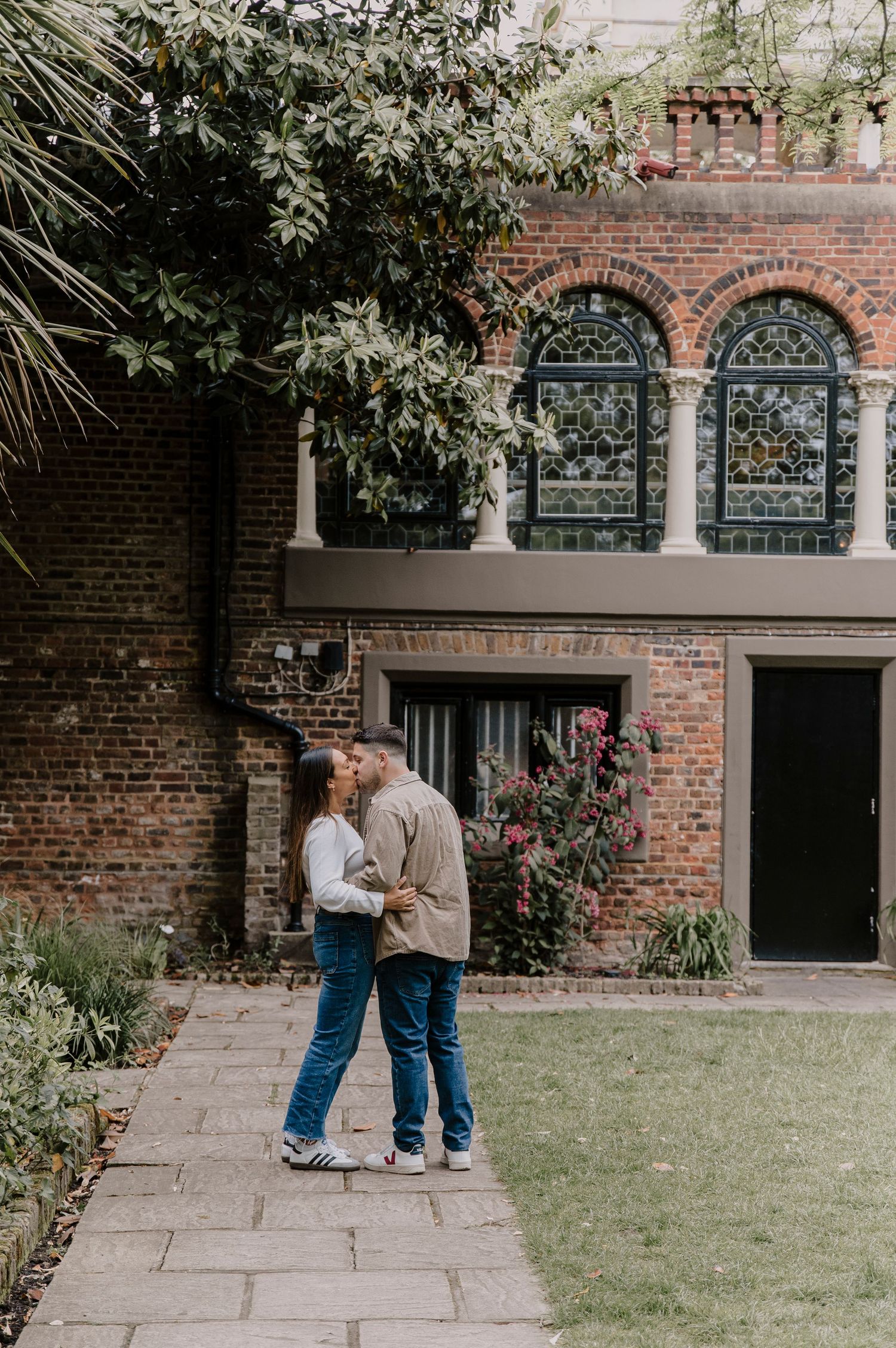 A couple shares an intimate moment together in a courtyard with brick walls and arched windows.