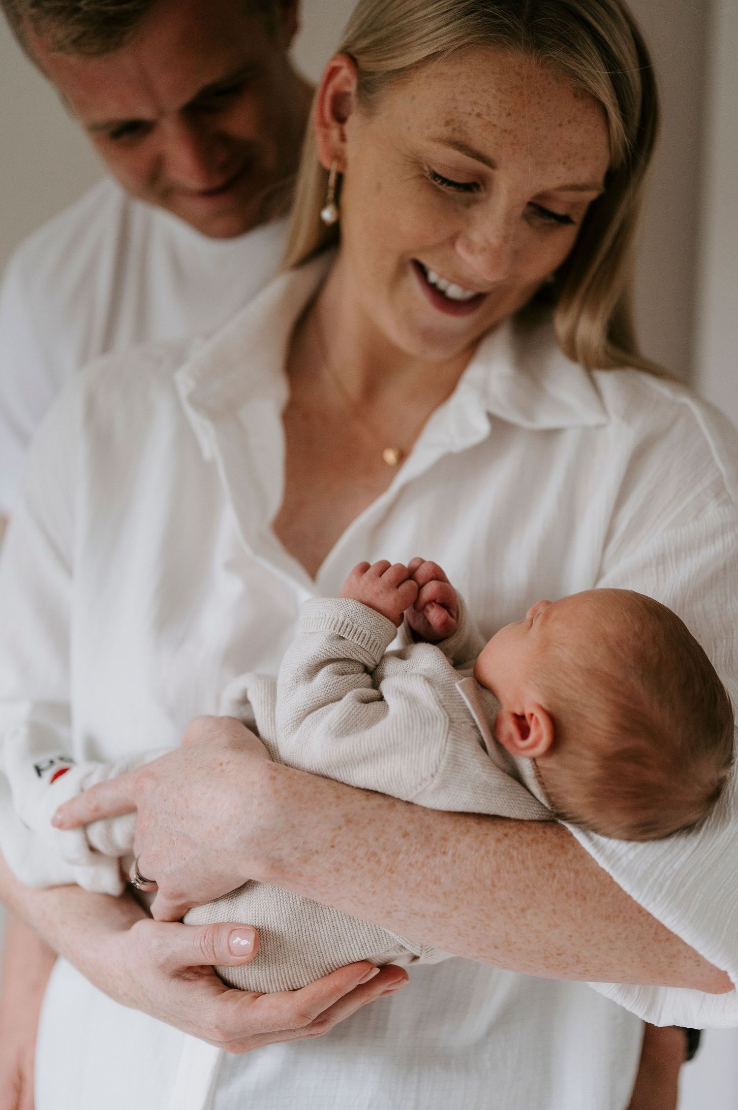 A tender moment between parent and newborn baby in white clothing against neutral background.