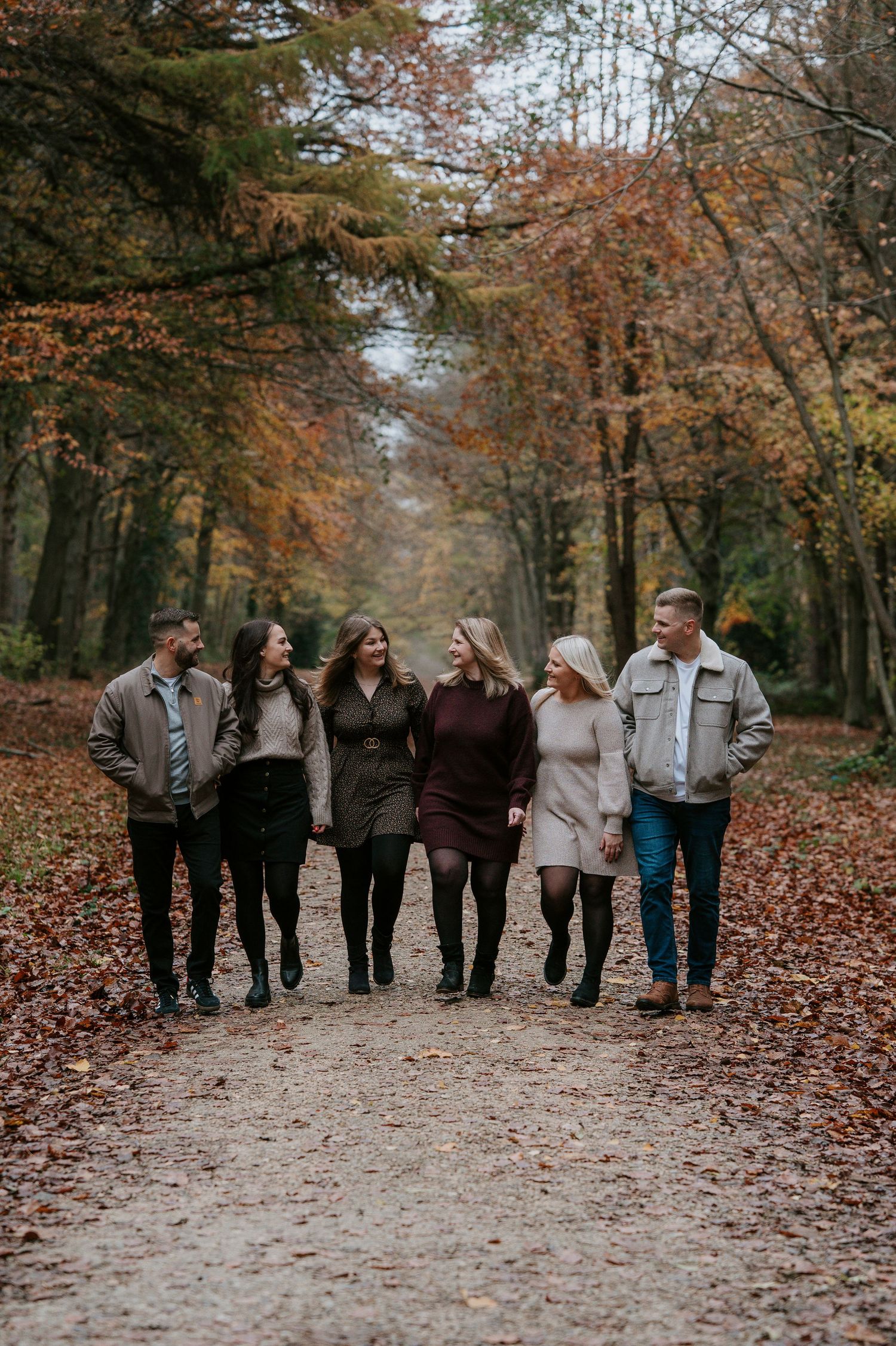 A group walks together on a leaf-covered forest path during autumn with trees displaying colorful fall foliage.