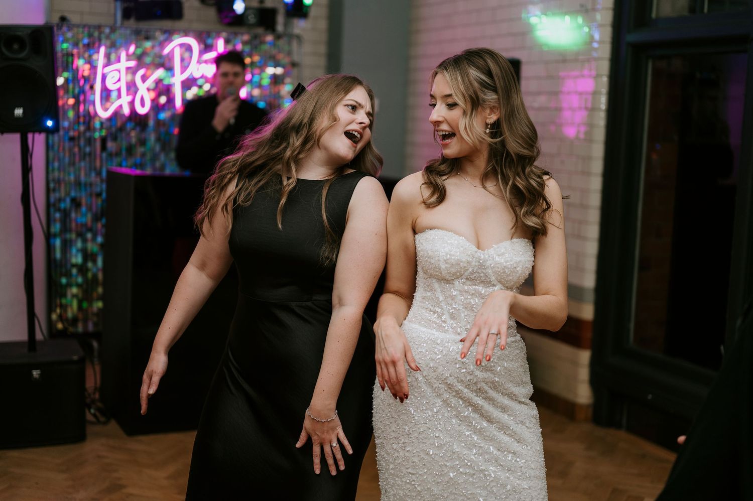 Wedding guests dancing under colorful neon lights at an indoor reception venue.